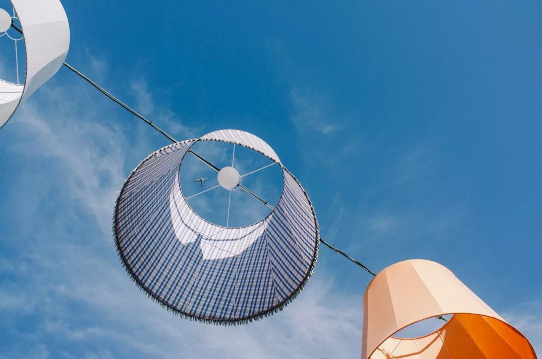 Drei große Lampenschirme hängen an einem Draht vor einem blauen Himmel, durch die Mitte des gestreiften Lampenschirms ist ein kleines Flugzeug zu sehen - ein Hinweis auf die innovativen Vorteile von Solarstrom fürs Zuhause.