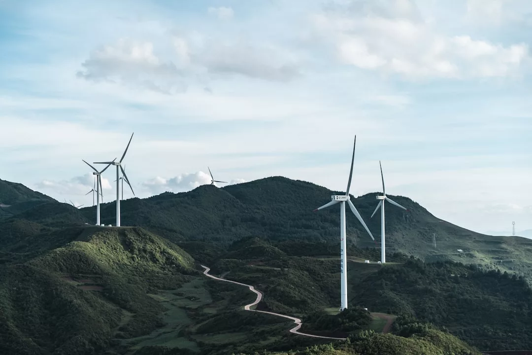 Windkraftanlagen, Symbole für nachhaltige Energie und Vorteile der Windkraft, stehen auf grünen Hügeln unter einem teils bewölkten Himmel, während sich im Vordergrund eine kurvenreiche Straße schlängelt.