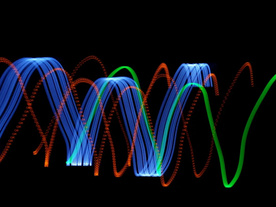 Abstrakte Lichtspuren, die an Tontechnik erinnern, bilden wellenförmige blaue, orangefarbene und grüne Linien vor schwarzem Hintergrund und erinnern an den visuellen Rhythmus der Frequenzanhebung.