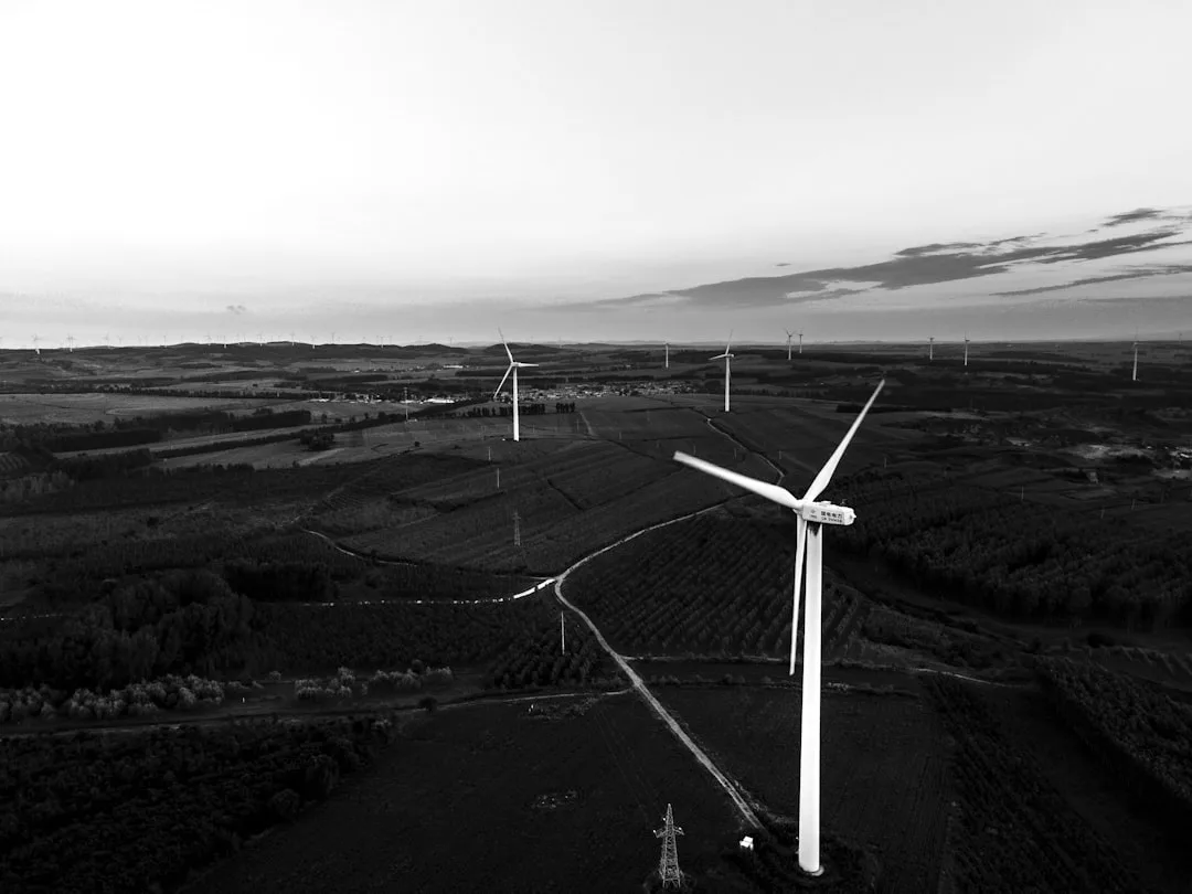Luftaufnahme von mehreren Windkraftparks, die sich über eine ländliche Landschaft mit Feldern und fernen Hügeln unter einem bewölkten Himmel erstrecken und innovative Energielösungen für die Zukunft hervorheben.
