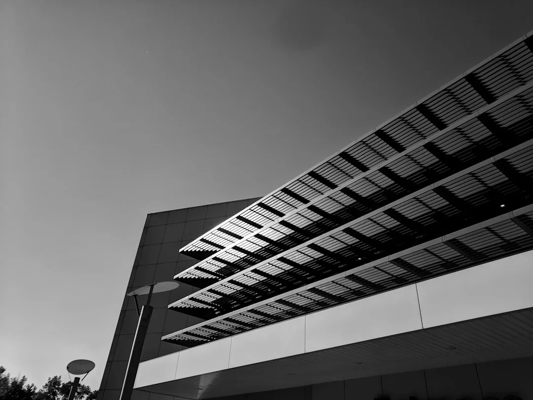 Ein modernes Gebäude mit horizontalem Schattenwurf, fotografiert aus einem niedrigen Winkel in Schwarz-Weiß unter klarem Himmel, steht beispielhaft für effiziente Lösungen und innovative Solarenergiespeicher in zeitgemäßer Architektur.