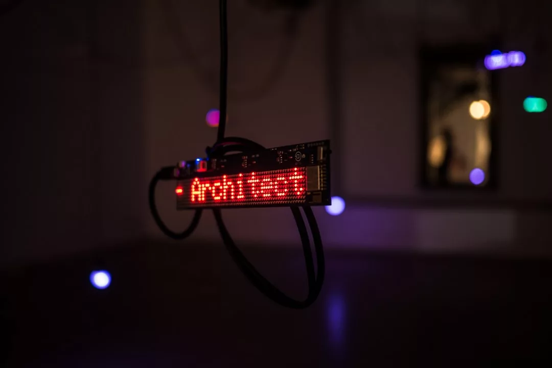Eine digitale LED-Anzeige mit der roten Aufschrift "Architects" hängt an Kabeln in einem schwach beleuchteten Raum und verbindet Digitale Kunst mit innovativem Design.