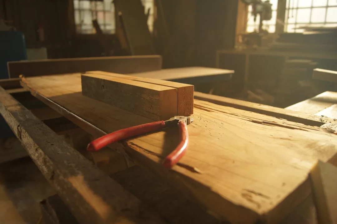 Eine Zange mit rotem Griff liegt auf einer rauen Holzwerkbank mit zwei rechteckigen Holzklötzen, bereit für kreative Ideen und DIY-Projekte in einer sonnenbeschienenen Zuhause-Werkstatt.