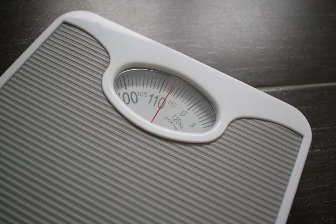 Eine Nahaufnahme einer mechanischen Personenwaage, die auf einer grauen, strukturierten Oberfläche ein Gewicht von etwa 110 Kilogramm anzeigt, ideal für die Verfolgung von Fortschritten auf dem Weg zum Ziel oder für Gewichtsverlust-Tipps.