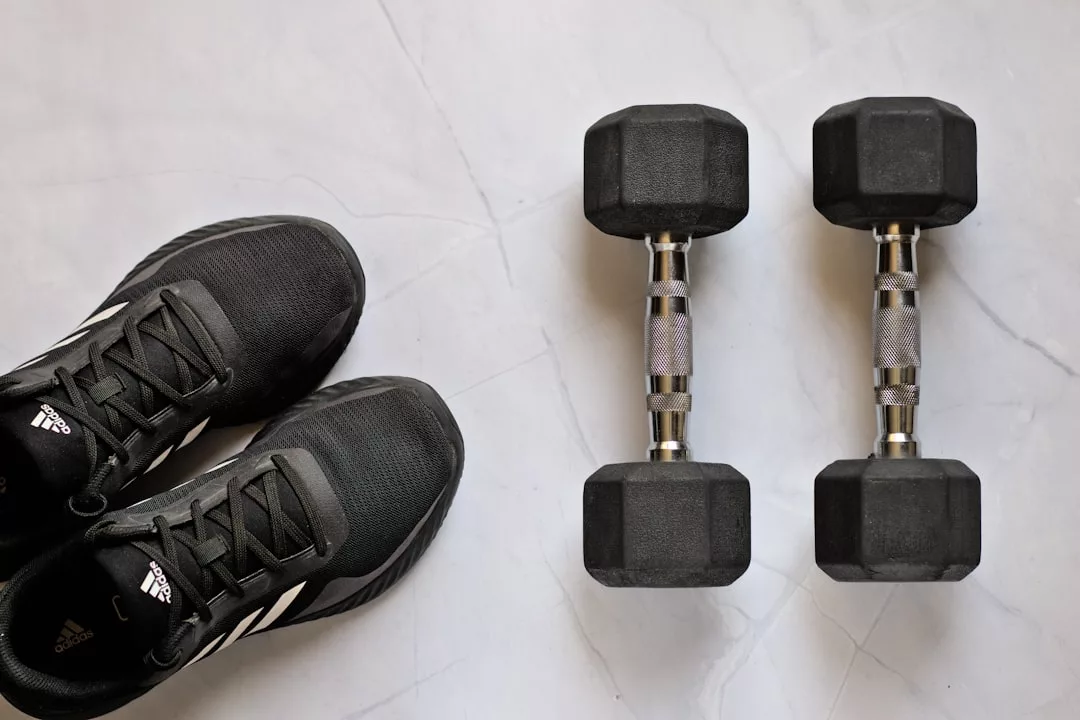 Ein Paar schwarze Sportschuhe stehen neben zwei schwarzen sechseckigen Hanteln auf einem hellen Marmorboden - perfekt für dein Home-Workout und effektive Routinen.