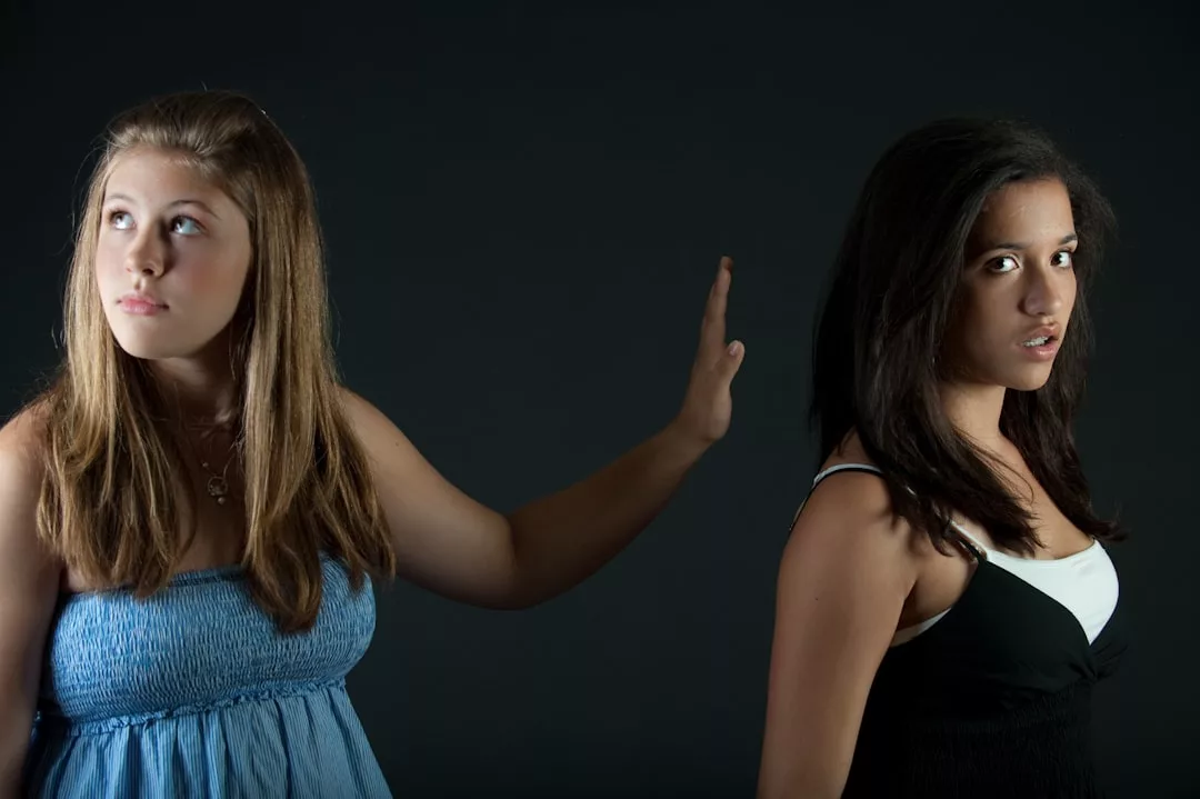 Zwei junge Frauen stehen Rücken an Rücken vor einem dunklen Hintergrund. Die eine streckt ihre Hand aus, als wolle sie die andere aufhalten, die ihr über die Schulter schaut. Beide haben einen ernsten Gesichtsausdruck und halten einen Moment von erfolgreicher Kommunikation und Konfliktgesprächen fest.