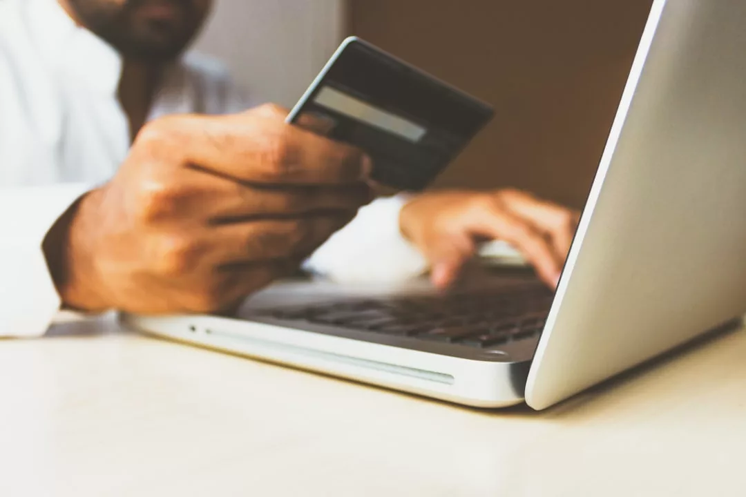 Eine Person hält eine Kreditkarte in der einen Hand, während sie mit der anderen auf einem Laptop tippt. Dies verdeutlicht die effektive Nutzung von elektronischem Bezahlen und Online-Shopping.