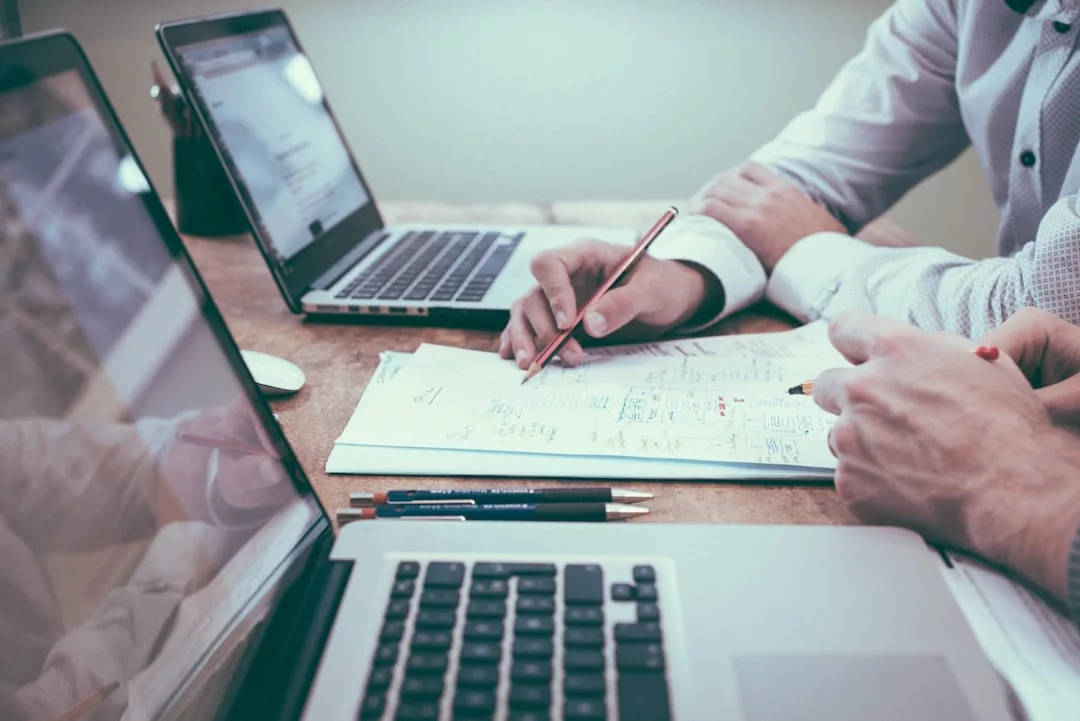 Zwei Personen arbeiten gemeinsam an einem Schreibtisch mit Laptops, schreiben mit Stiften Notizen auf Papier und besprechen Dokumente für effektive Nachhilfe.