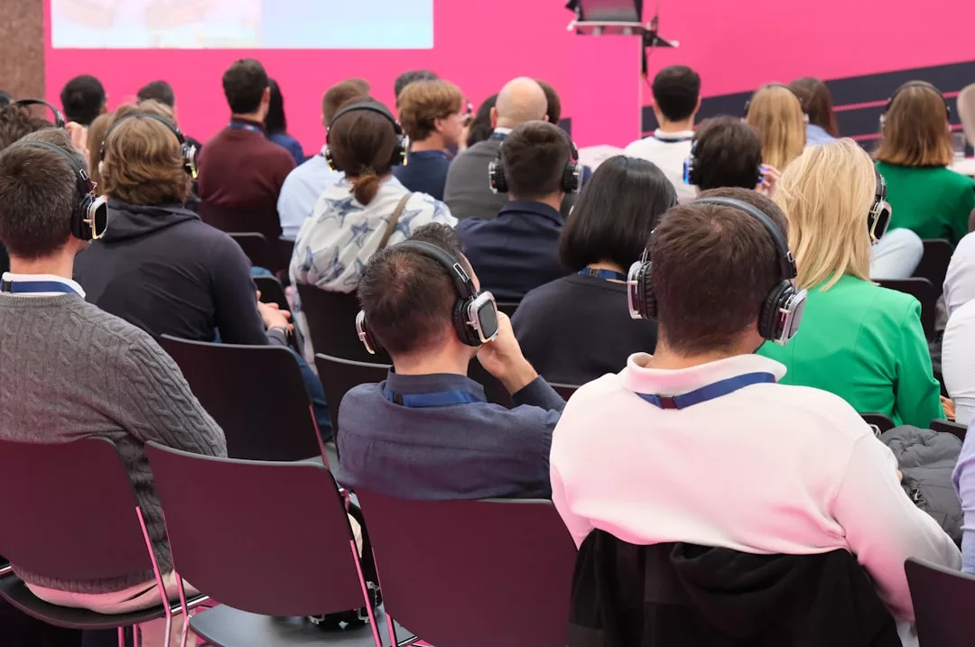 Eine Gruppe von Personen, die in Reihen sitzen, Kopfhörer tragen und auf eine Bühne mit rosa Hintergrund blicken. Sie nehmen an einem Kommunikationstraining zur Verbesserung ihrer effektiven Kommunikation und ihres beruflichen Erfolgs teil.