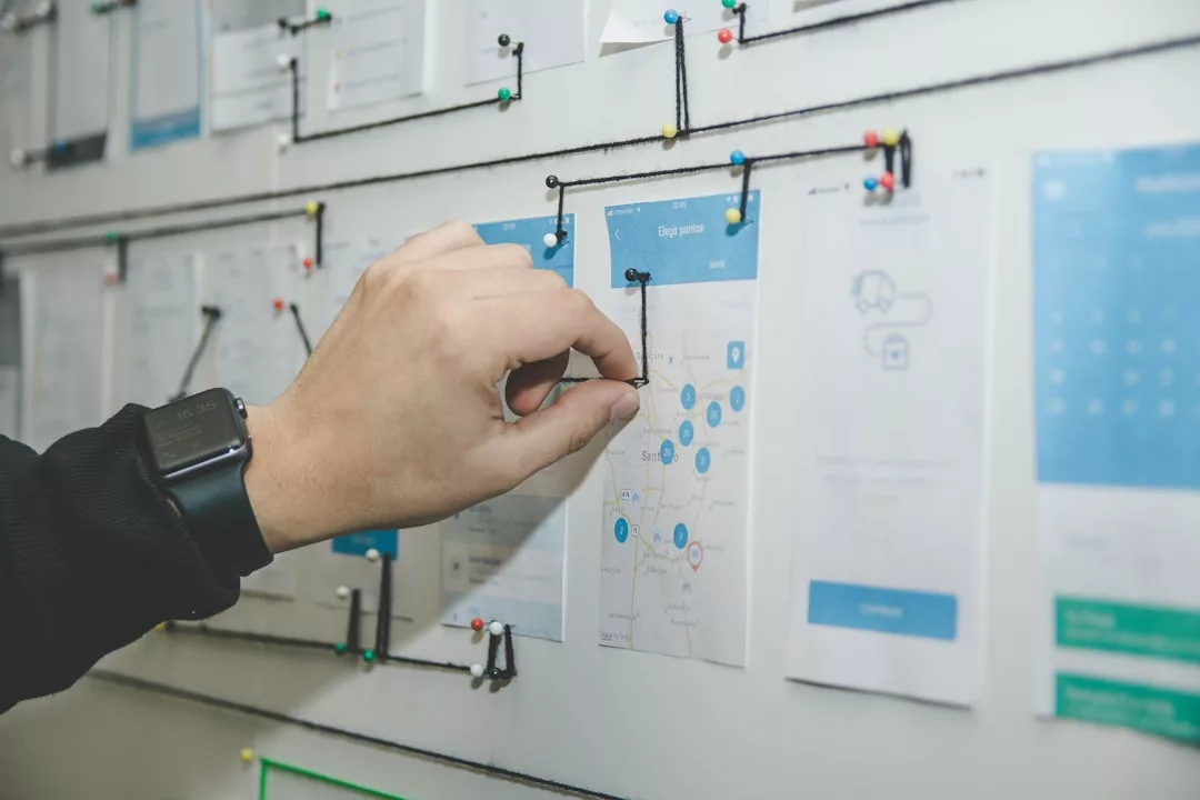 Eine Person verbindet Stecknadeln mit einer Schnur auf einer Tafel, auf der Papierdokumente, Diagramme und Tabellen abgebildet sind, um Informationen für ein effektives Risikomanagement im Unternehmen visuell zu organisieren.