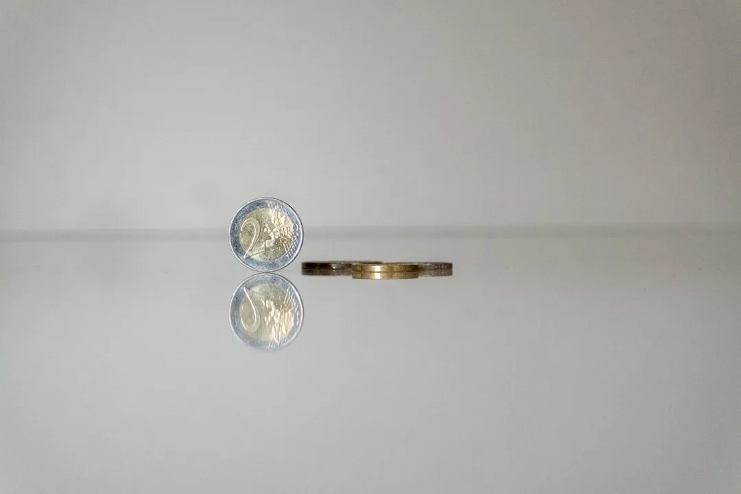 Eine 2-Euro-Münze steht aufrecht neben zwei horizontalen Münzen auf einer spiegelnden Oberfläche und symbolisiert effektive Schuldenmanagement-Strategien vor einem schlichten Hintergrund.