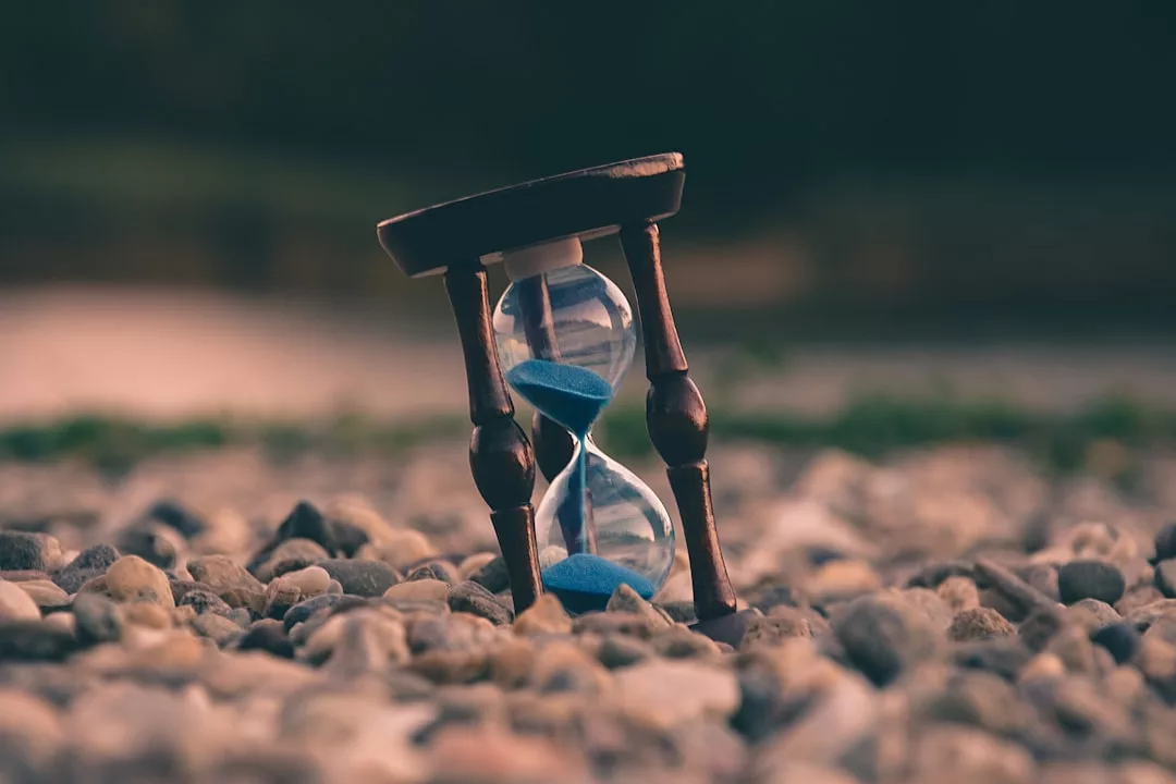 Eine mit blauem Sand gefüllte Sanduhr, die Zeitmanagement und Produktivität symbolisiert, ist auf die Seite gekippt und ruht auf einer mit kleinen Steinen bedeckten Fläche.