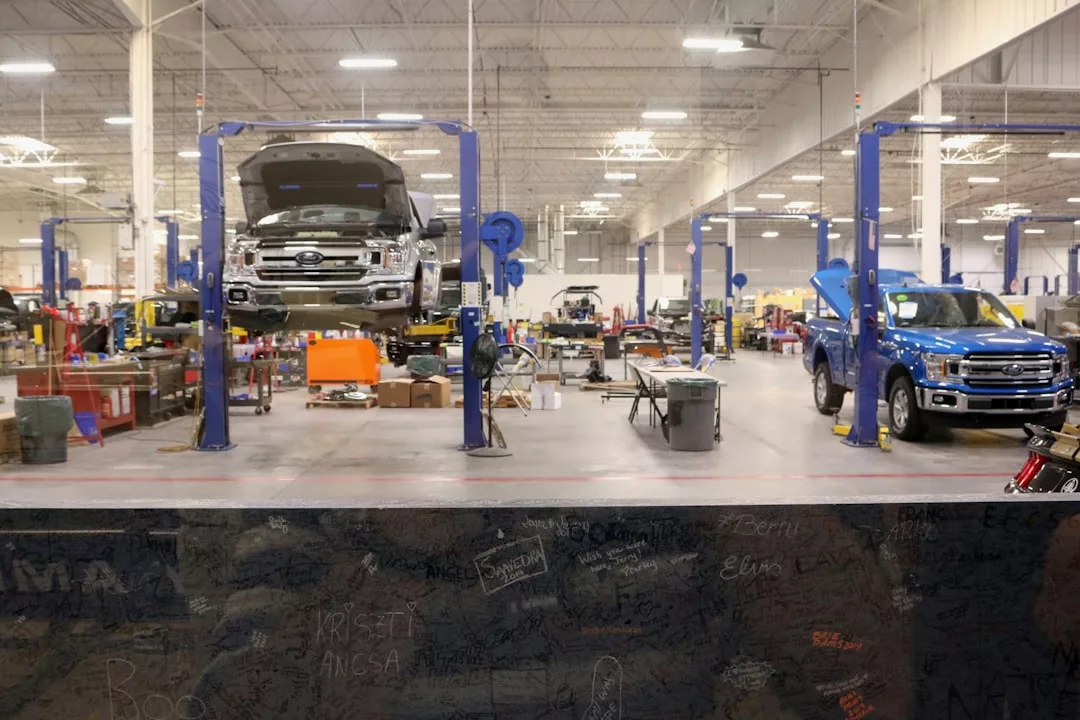 Große Autoreparaturwerkstatt mit mehreren Fahrzeugen auf Hebebühnen, einige mit offenen Motorhauben, umgeben von Werkbänken, Werkzeugen und Geräten unter heller Deckenbeleuchtung - perfekt, um neue Tipps und Tricks des Handwerks zu lernen.