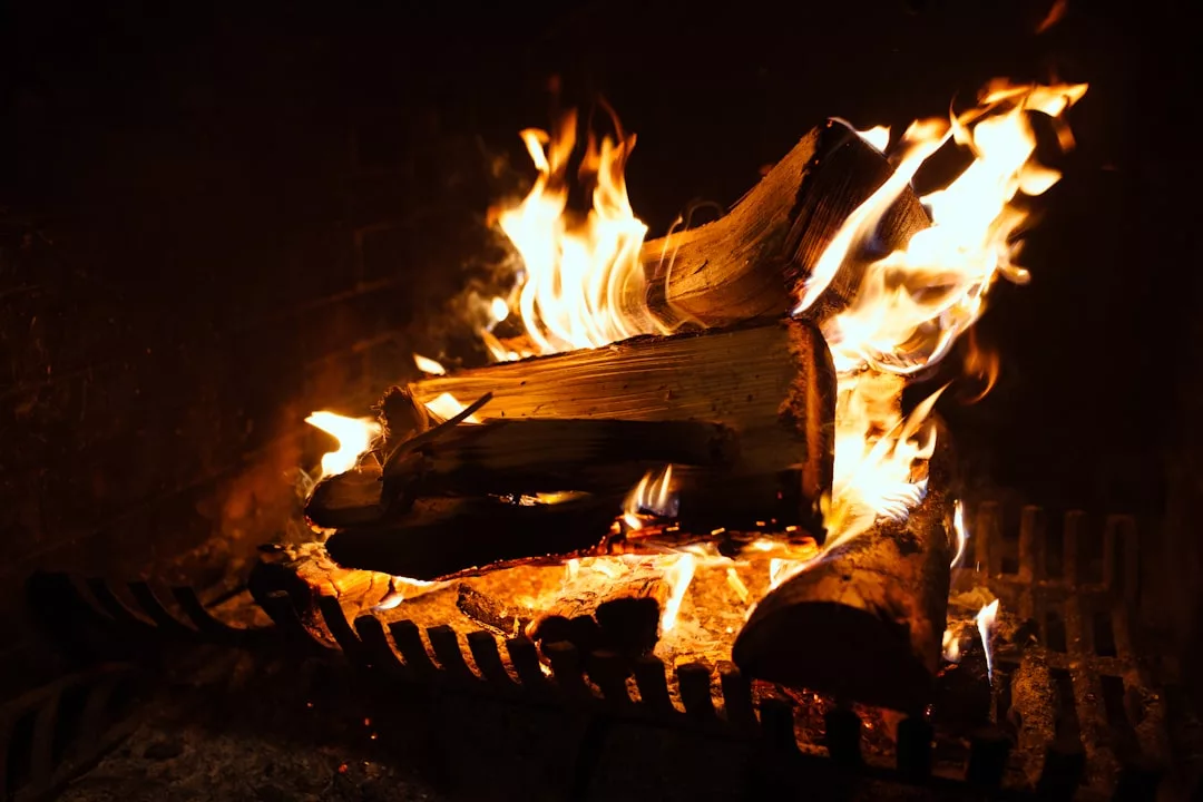 Brennende Holzscheite in einem Kamin mit hellen Flammen und Glut auf einem Metallrost schaffen eine effiziente Wärmequelle für behagliche Wärme.