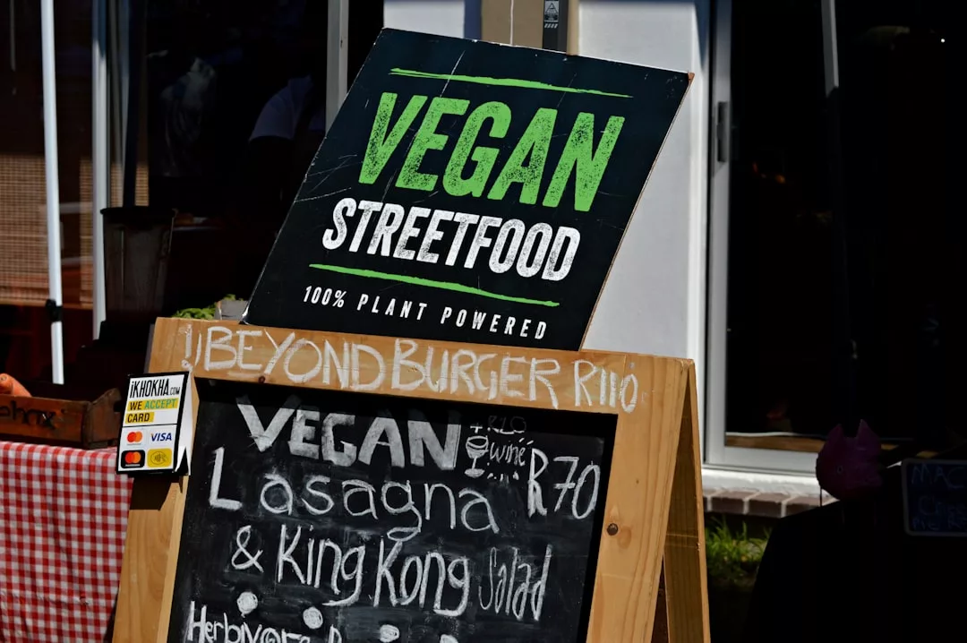 Auf einem Schild steht "VEGAN STREETFOOD 100% PLANT POWERED" über einer Speisekarte, auf der vegane Lasagne, King Kong Salat und ein Beyond Burger aufgeführt sind - perfekt für Tipps und Grundlagen der veganen Ernährung.