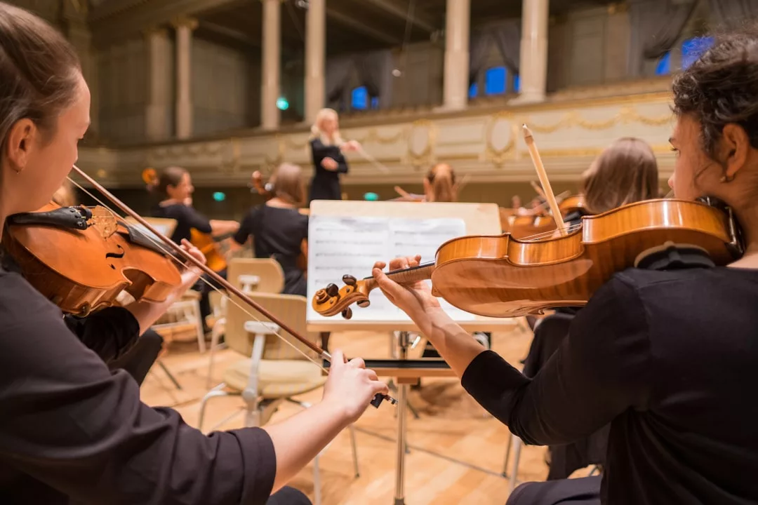 Musiker spielen Geigen in einem Orchester, lesen Noten und werden von einem Dirigenten auf der Bühne eines Konzertsaals dirigiert - eine ideale Einführung in Klassische Musik für Anfänger.