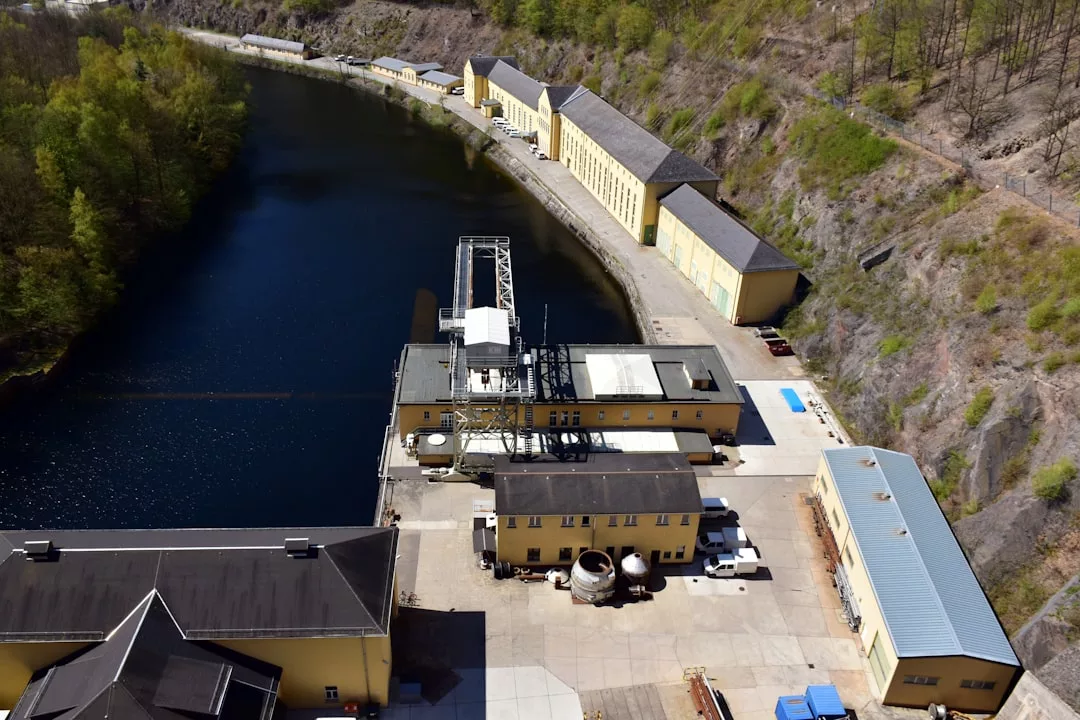 Luftaufnahme eines Wasserkraftwerkskomplexes mit gelben Gebäuden an einem Fluss, umgeben von Bäumen und felsigem Gelände, zur Veranschaulichung nachhaltiger Lösungen für die Energieerzeugung.
