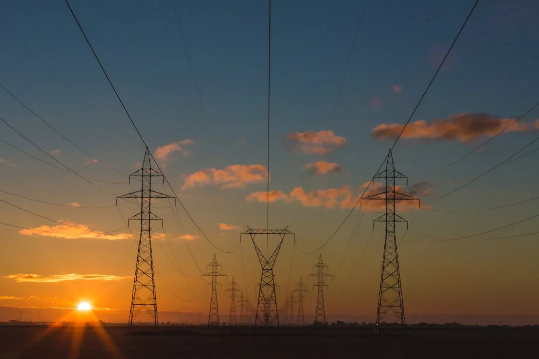 Hochspannungsleitungen und Sendemasten ziehen sich bei Sonnenuntergang durch die Landschaft und symbolisieren den Energiefluss und das Streben nach mehr Energieeffizienz unter einem wolkenlosen Himmel.