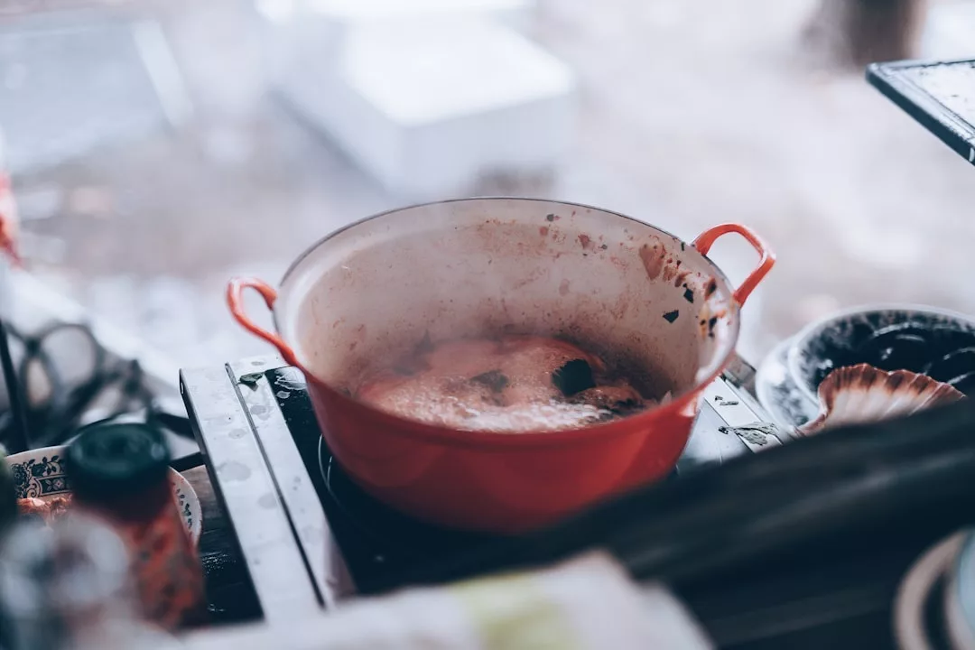 Ein roter Topf mit zwei Griffen steht auf dem Herd und köchelt, während Dampf aufsteigt - wie die Wärme, die Sie nach dem Genuss energiegeladener Smoothies aus Ihren Lieblings-Smoothie-Rezepten spüren.