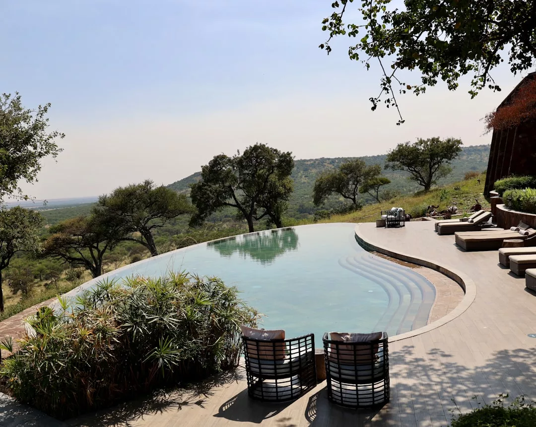 Ein Infinity-Pool mit Liegestühlen überblickt eine üppige, hügelige Landschaft unter einem klaren Himmel - ein idealer Ort, um nach Safari-Reisen und Welt entdecken zu entspannen.