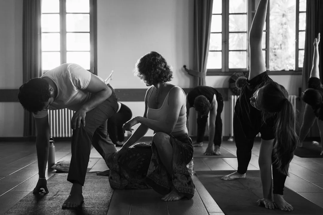 In einem gut beleuchteten Studio mit großen Fenstern führt ein Yogalehrer eine Gruppe von Menschen durch verschiedene Dehnungshaltungen und ermutigt sie, während ihrer Praxis Stärken zu entdecken.