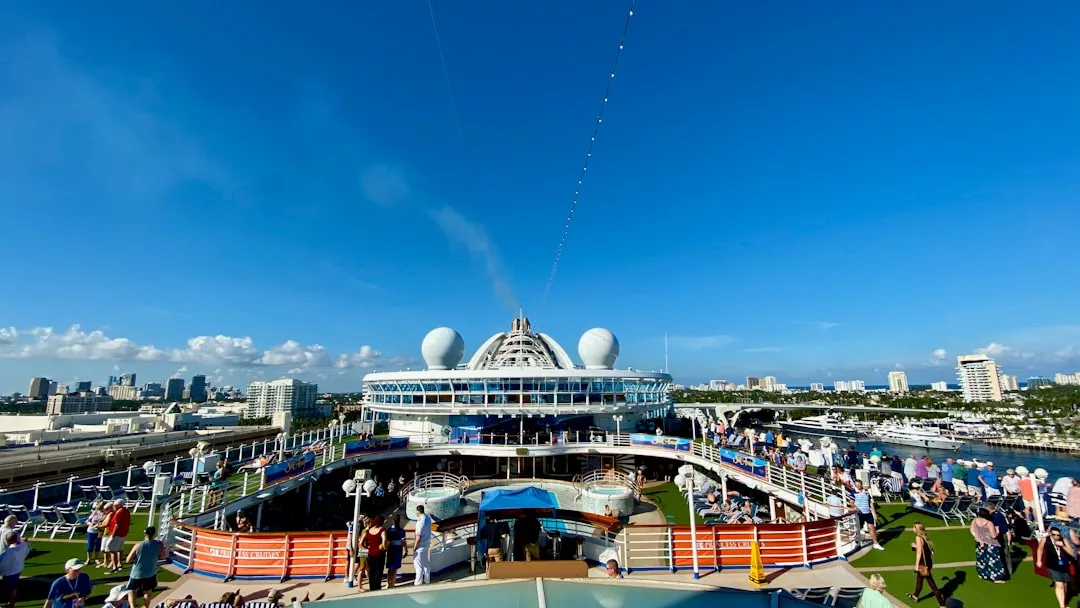 Genießen Sie den Blick vom Oberdeck einer Luxuskreuzfahrt, mit Menschen, die sich am Pool entspannen, und einer atemberaubenden Skyline der Stadt im Hintergrund unter einem klaren blauen Himmel.