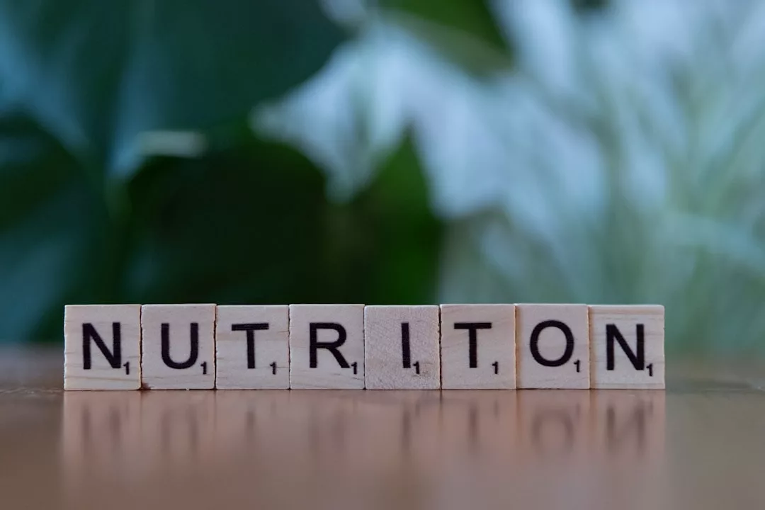 Die hölzernen Scrabble-Kacheln buchstabieren "NUTRITION" auf einer flachen Oberfläche vor einem unscharfen grünen Hintergrund - perfekt zur Illustration von Themen rund um gesunde Ernährung oder als Ernährungsratgeber.