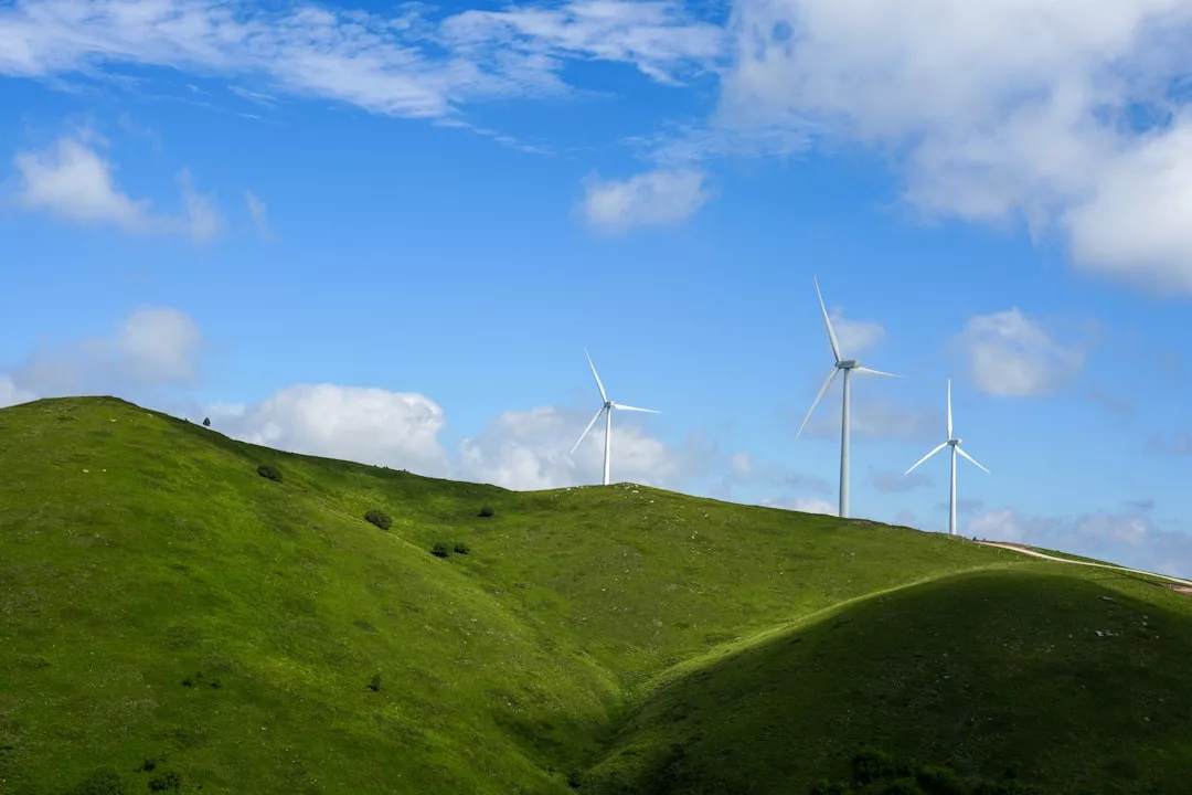 Drei Windräder stehen auf grünen Hügeln unter einem blauen Himmel mit vereinzelten weißen Wolken und symbolisieren aktuelle Trends im Bereich erneuerbare Energien.