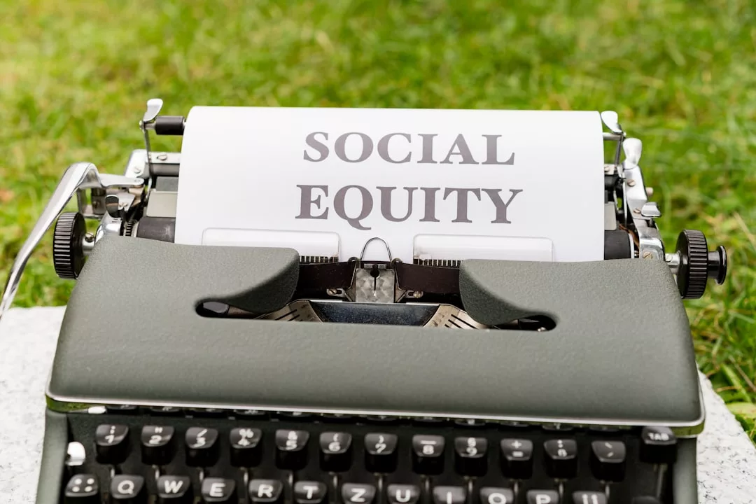 Eine Schreibmaschine mit einem Blatt Papier, auf dem "SOCIAL EQUITY" steht, liegt auf einer Wiese und erinnert an die Themen der Verantwortung, die in Investmentfonds und ETFs zu finden sind.
