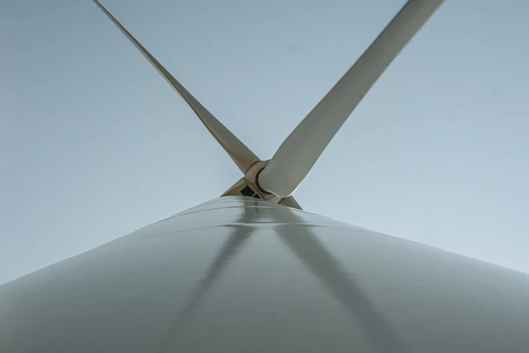 Nahaufnahme eines Windturbinenturms und seiner beiden sichtbaren Flügel vor einem klaren Himmel, der innovative Maßnahmen zur Förderung von Windenergie hervorhebt.