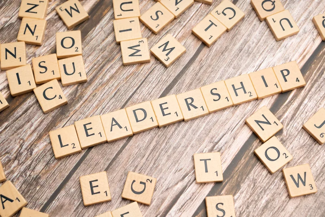 Auf einem Tisch liegen hölzerne Buchstabenplättchen mit der Aufschrift "LEADERSHIP" und andere verstreute Plättchen, die die Herausforderungen und Anforderungen symbolisieren, denen Führungspositionen täglich begegnen.