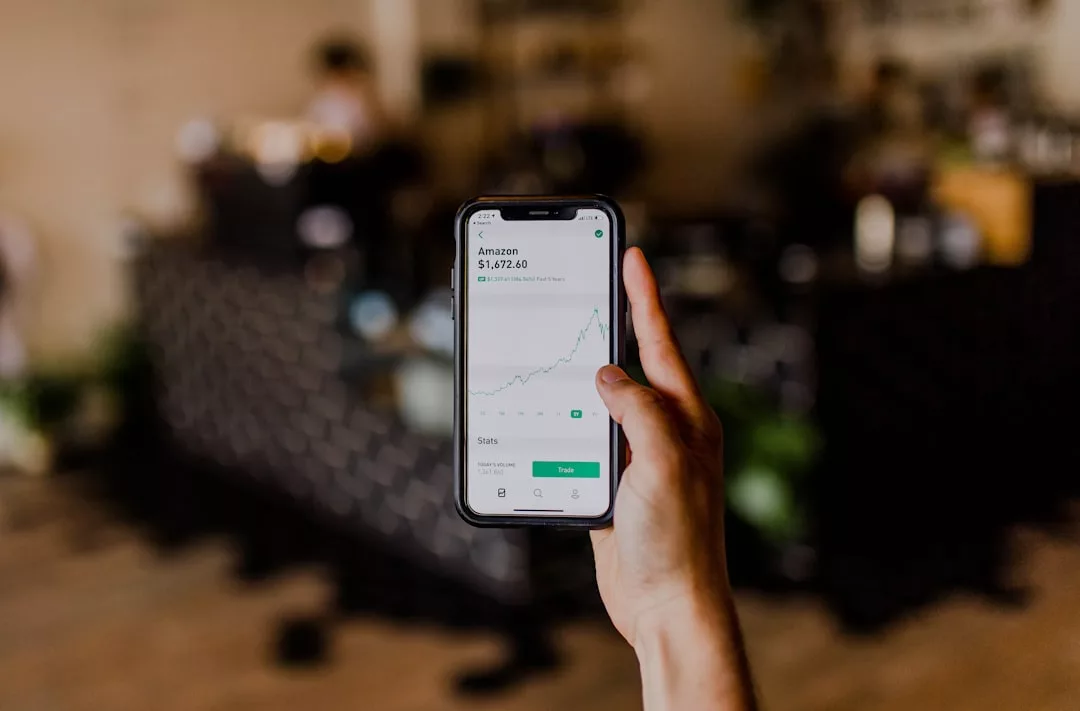 Eine Person hält ein Smartphone in der Hand, auf dem eine Aktienhandels-App mit einem aufwärtsgerichteten Amazon-Aktienchart angezeigt wird, auf dem Geldanlage-Strategien in Krisenzeiten und der aktuelle Kurs von 3.172,60 $ zu sehen sind.
