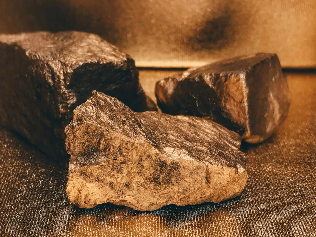 Drei raue, dunkelbraune Felsen mit strukturierter Oberfläche sind auf einem glitzernden, goldenen Hintergrund platziert und unterstreichen die Attraktivität von Gold als sichere Investition.