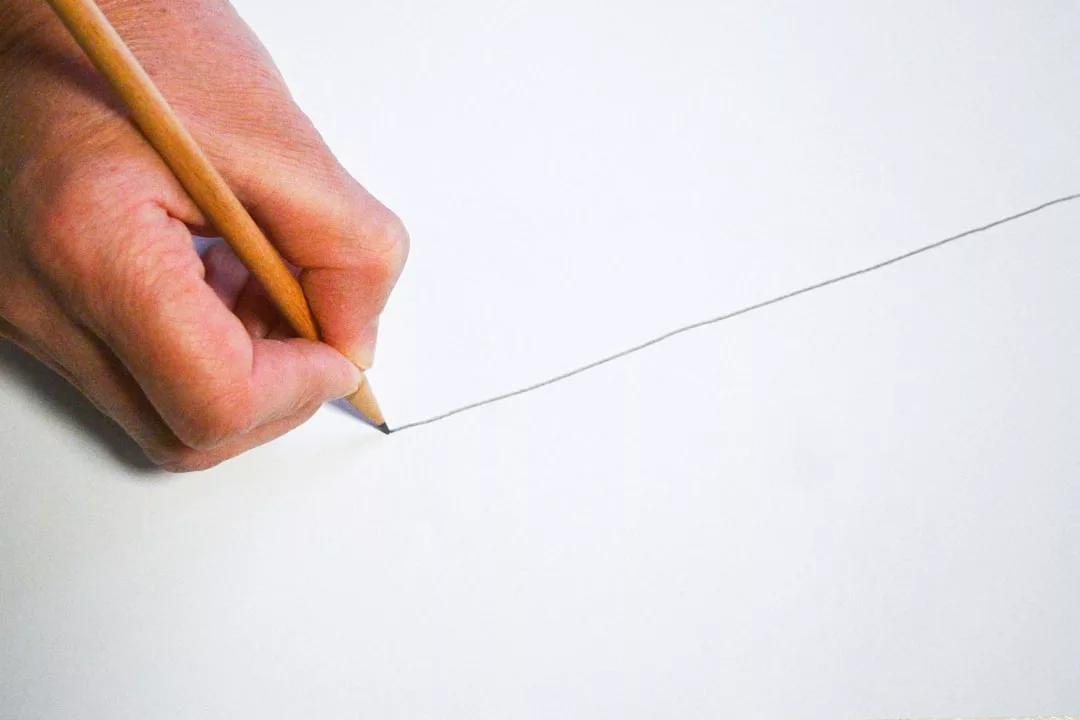 Eine Hand hält einen Bleistift und zeichnet eine gerade diagonale Linie auf ein weißes Blatt Papier - ein Symbol dafür, wie wichtig es ist, in persönlichen Beziehungen Grenzen zu setzen.
