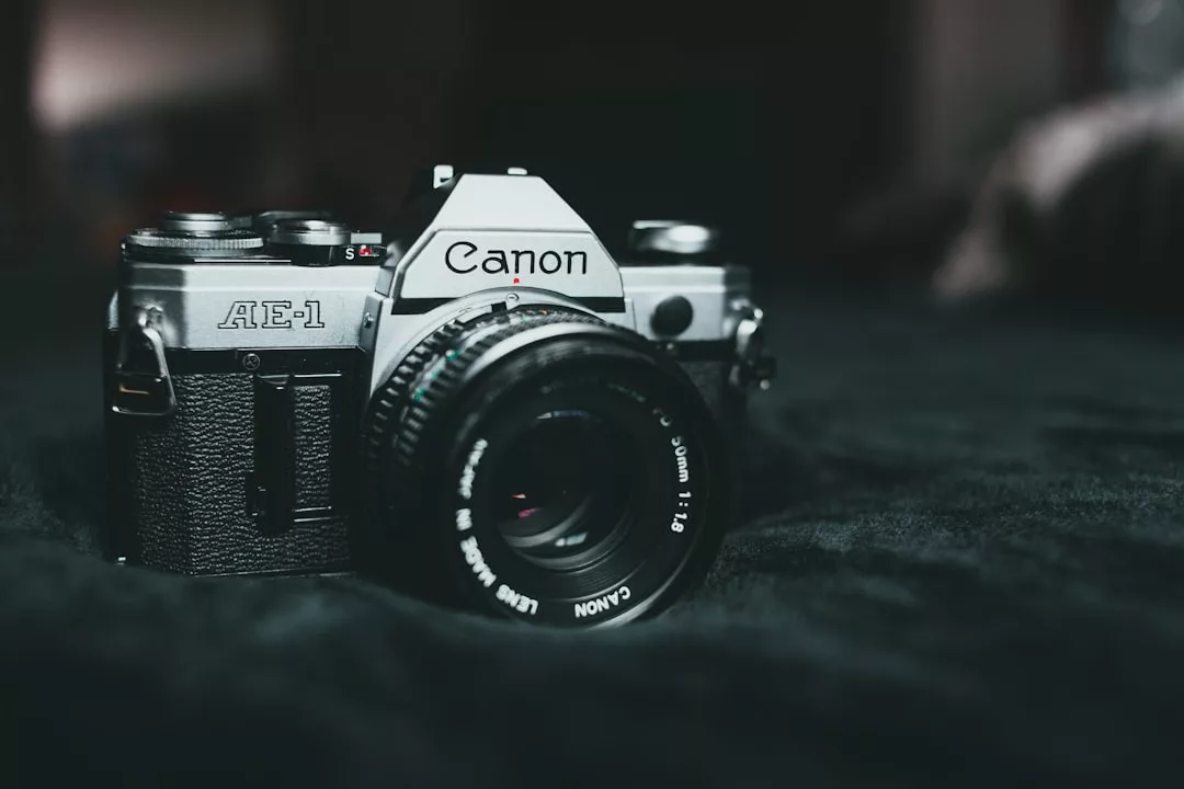 Eine Canon AE-1 Filmkamera mit einem 50-mm-Objektiv ruht auf einer dunklen, strukturierten Oberfläche bei gedämpfter Beleuchtung und fängt die Grundlagen klassischer Fotografie ein.