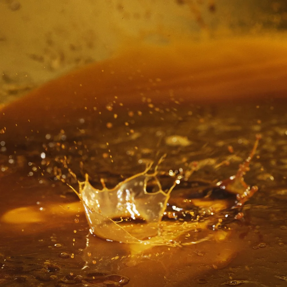 Ein Tropfen Sérum Vivant von Biologique Recherche fällt in bernsteinfarbene Flüssigkeit