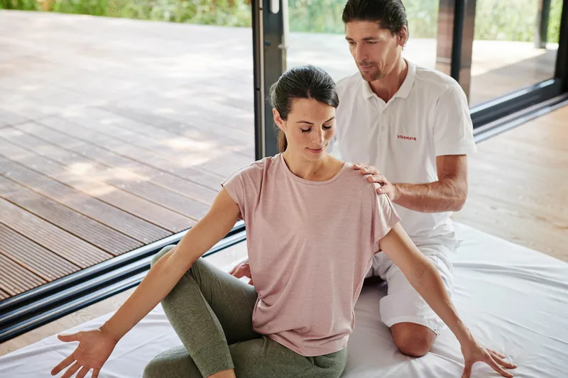 Yogastunde bei VIVAMAYR: Ein Lehrer korrigiert die Haltung einer Teilnehmerin auf der Matte