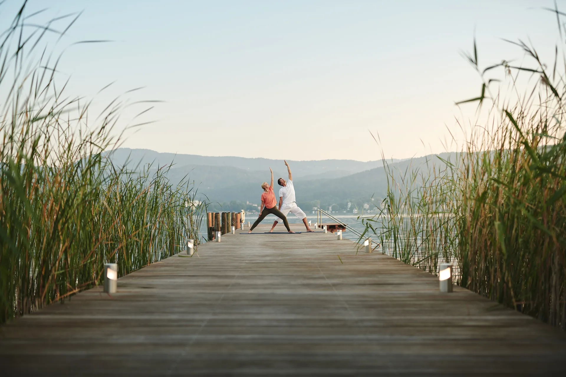 Yoga zu zweit auf einem langen Holzsteg zwischen Schilf, ein Motiv der VIVAMAYR Holistic Health Weeks