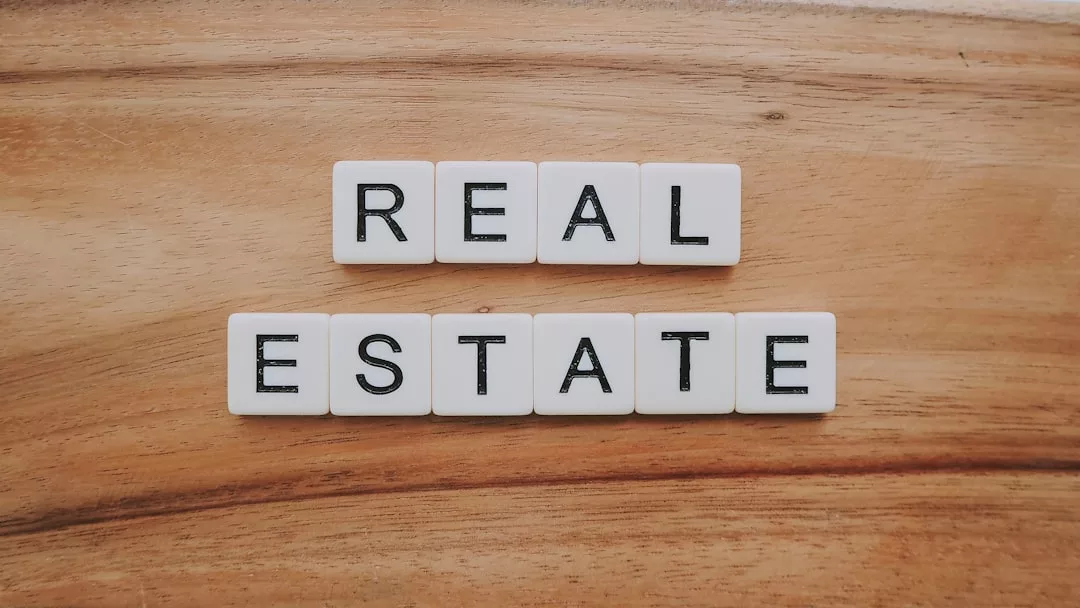 Weiße Buchstabenkacheln auf einer hölzernen Oberfläche buchstabieren in der obersten Zeile "REAL" und darunter "ESTATE" und symbolisieren damit Immobilien als wichtiges Element der Altersvorsorge.