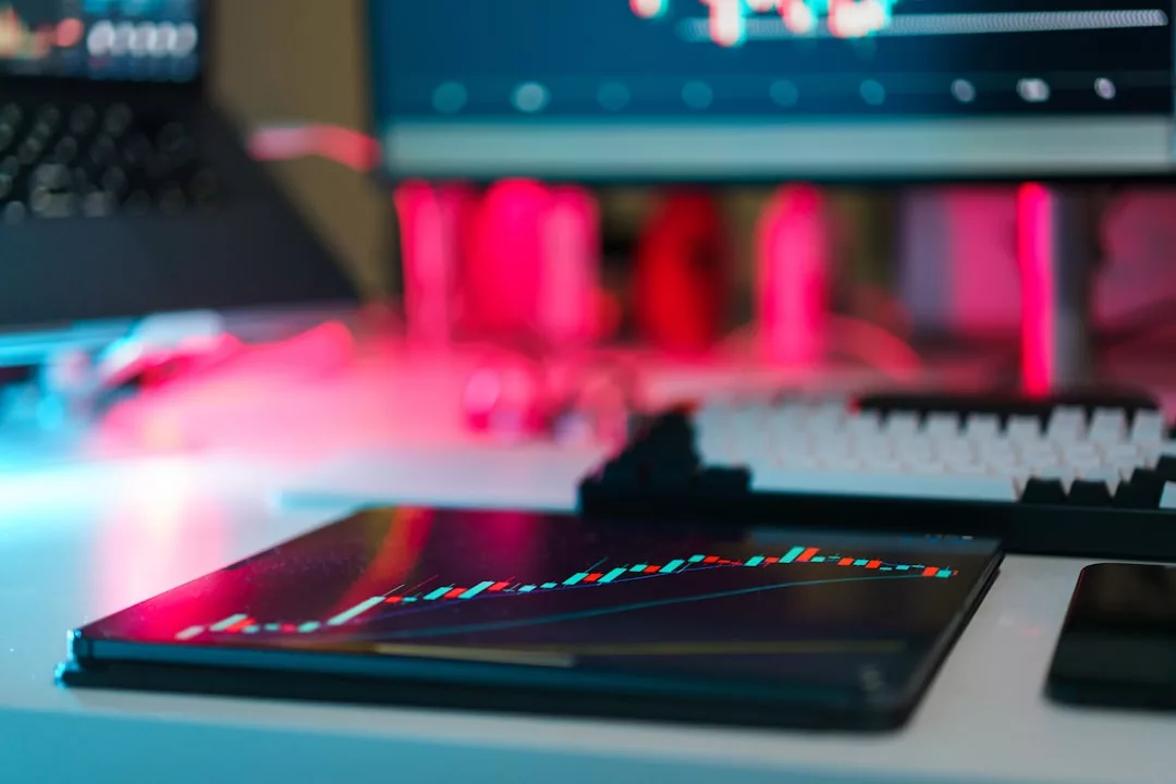 Ein digitales Tablet mit einem farbenfrohen Aktienchart liegt auf einem Schreibtisch in der Nähe einer Tastatur, auf der aktuelle Investment-Trends und Chancen hervorgehoben werden, mit Computermonitoren und roten Lichtern im Hintergrund.