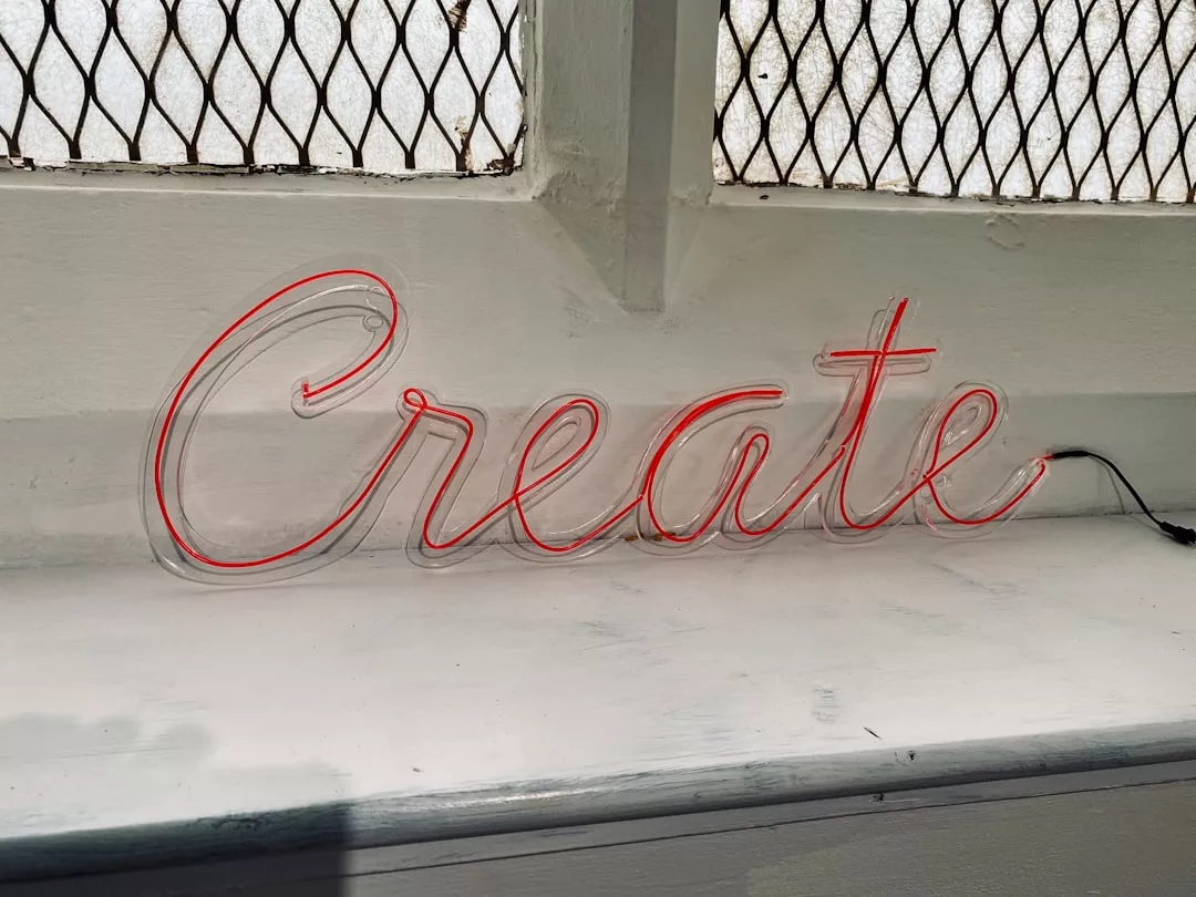 Eine Leuchtreklame in Schreibschrift mit dem Wort "Create" steht auf einer weißen Fensterbank, inspiriert zu kreativem Spiel und fördert die Kreativität der Kinder vor einem Fenster mit einem Drahtgitter.