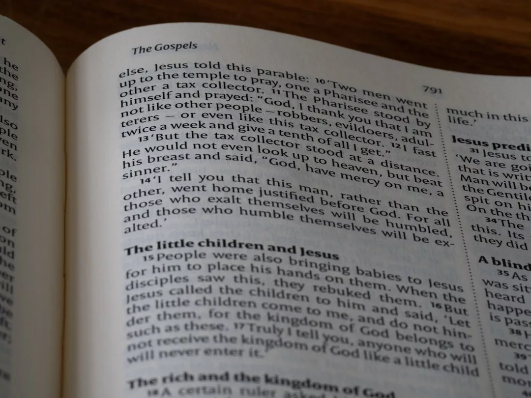 Eine aufgeschlagene Bibel zeigt Texte aus dem Abschnitt Evangelien, mit sichtbaren Passagen zum Gleichnis vom Pharisäer und dem Zöllner, und bietet biblische Tipps zur Demut und Konfliktlösung für Kinder.