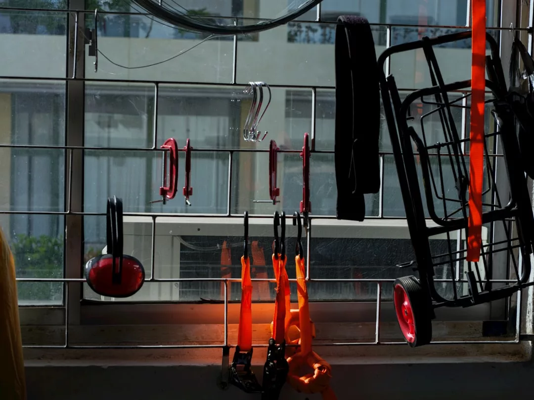 Mehrere Küchenutensilien, darunter eine Zange und ein Schneebesen, hängen an einem Metallgitter vor einem sonnenbeschienenen Fenster, aus dem ein Wohnhaus zu sehen ist - eine kreative Aufbewahrung für ein ordentliches Zuhause.