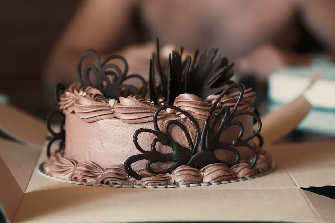 Ein köstlicher Kuchen mit dekorativen Schokoladenstückchen und Strudeln, der in einer offenen Pappschachtel präsentiert wird - perfekt für Liebhaber kulinarischer Köstlichkeiten.