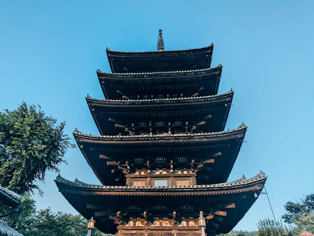 Eine traditionelle fünfstöckige Holzpagode steht vor einem strahlend blauen Himmel, umgeben von etwas Grün - ein bezaubernder Ort für Kulturtouristen, die kulturelle Schätze jenseits von Deutschland erkunden wollen.