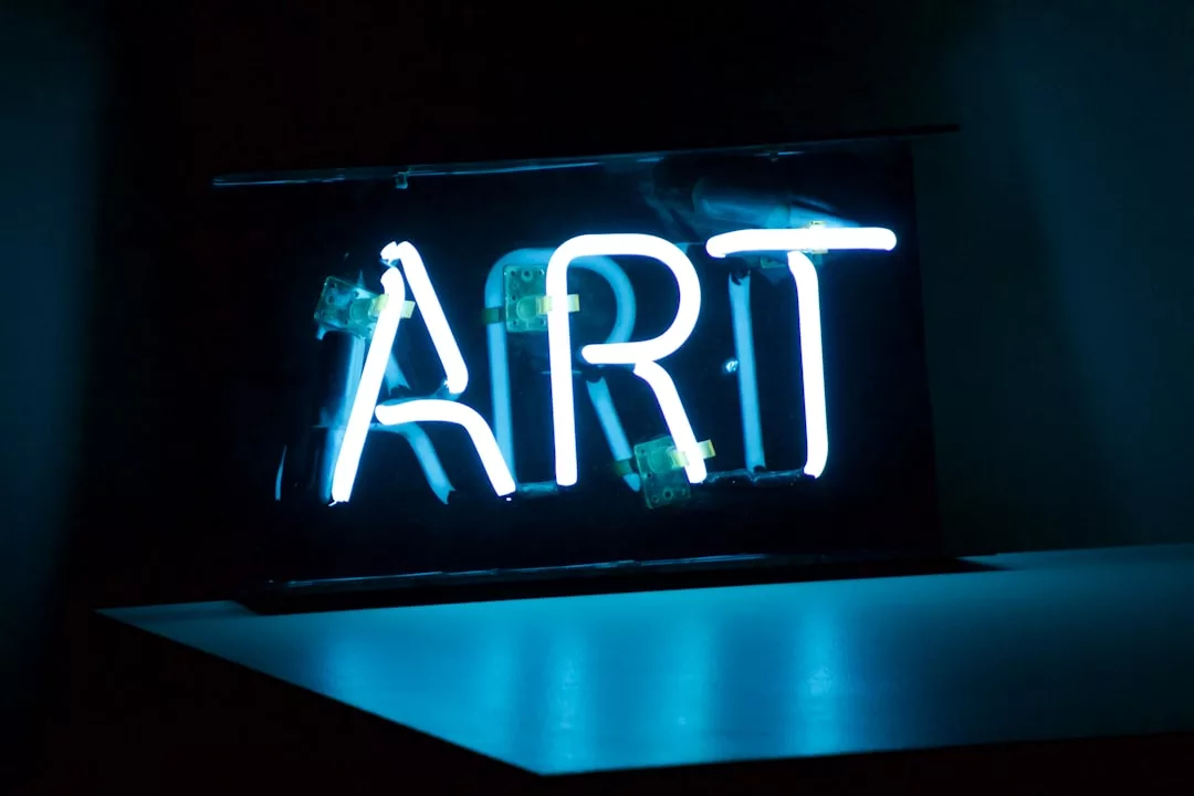 Eine Leuchtreklame mit dem Wort "ART" in leuchtend blauen Buchstaben leuchtet in einer dunklen Umgebung und erinnert an den lebendigen Geist des traditionellen Handwerks in Deutschland.