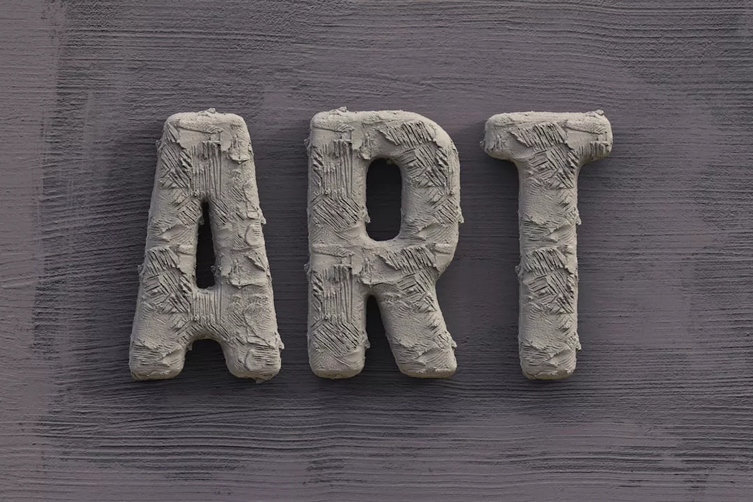 Das Wort "ART" steht in großen, strukturierten, grauen Buchstaben, die an Gips oder Beton erinnern, vor einem dunkelgrauen Hintergrund und erinnert an den Geist der Deutschen Kunstausbildung und an die klassischen Traditionen der formalen Kunstausbildung.