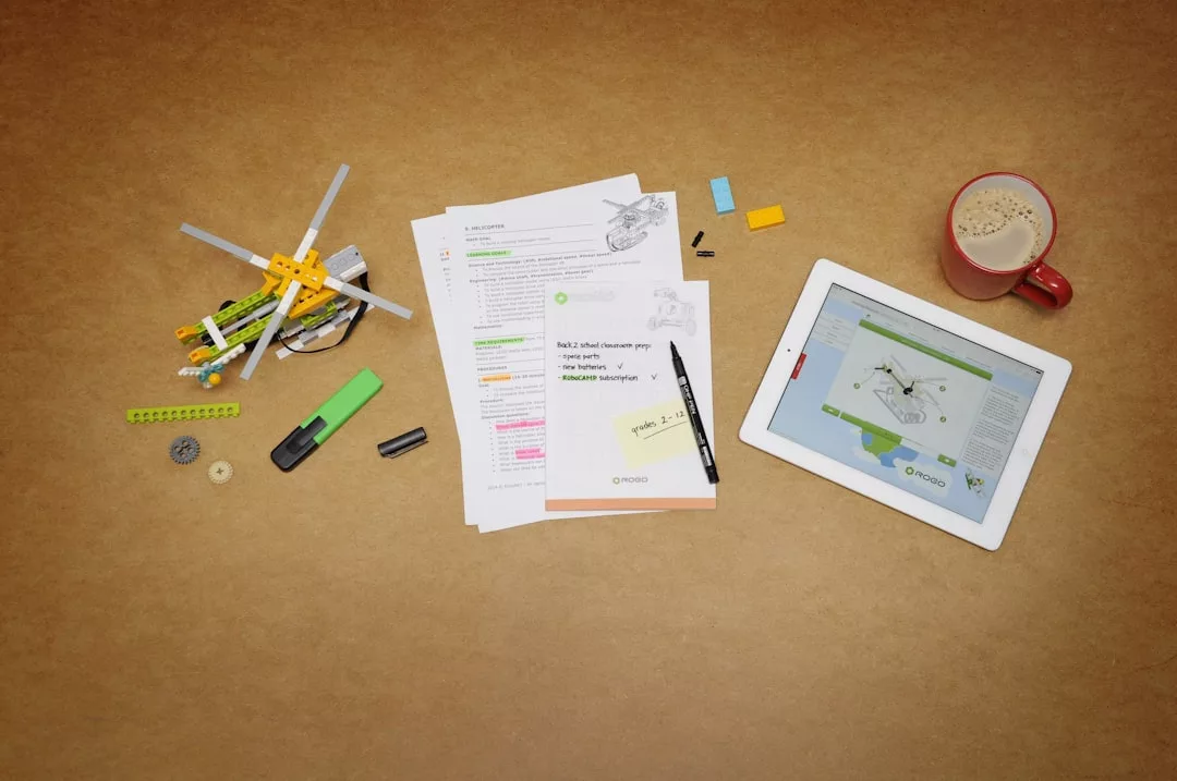 Ein Schreibtisch mit einem Spielzeug-Hubschraubermodell, Arbeitsblättern, einem schwarzen Stift, Textmarkern, einem iPad mit Diagrammen und einer roten Tasse mit einem heißen Getränk - ideal für Lernplan erstellen und effektive Strategien beim Lernen.