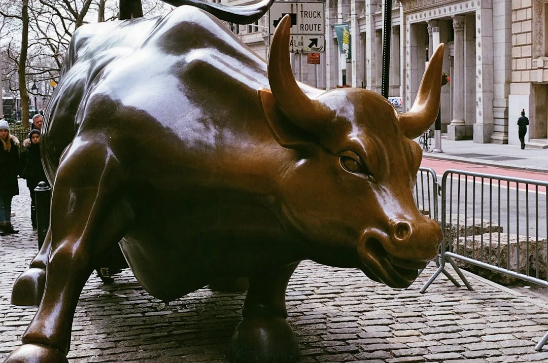 Eine große bronzene Stierstatue steht auf einer Kopfsteinpflasterstraße und symbolisiert Chancen und Herausforderungen in Zeiten der Marktvolatilität, während im Hintergrund Gebäude, Absperrungen und Fußgänger zu sehen sind.