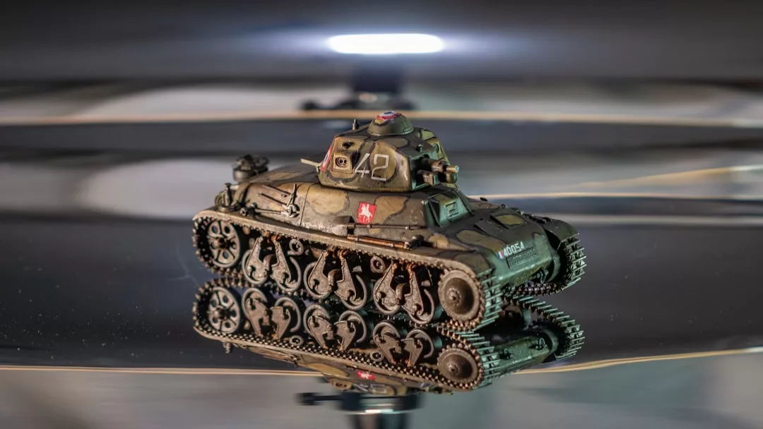 Ein kleiner Modellbau-Militärpanzer liegt auf einer spiegelnden Fläche, seine Details und Markierungen werden unter hellem Licht als Kunst dargestellt.